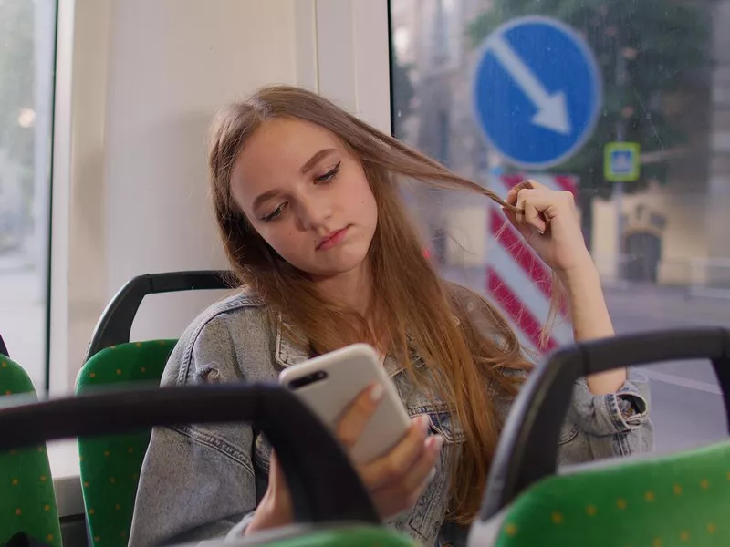 Woman playing on smartphone, chatting, texting, browsing social media while traveling by bus to city