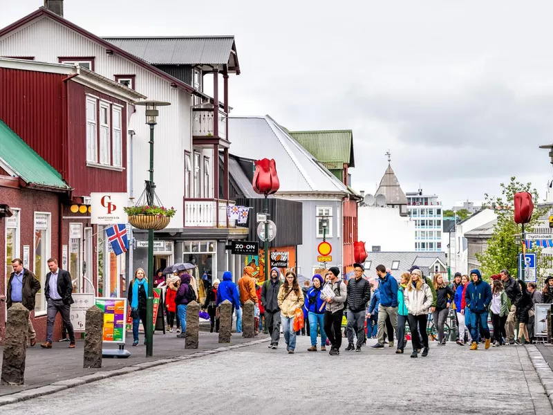 Many people tourists walking on street sidewalk in downtown center by stores shops restaurant with signs in summer