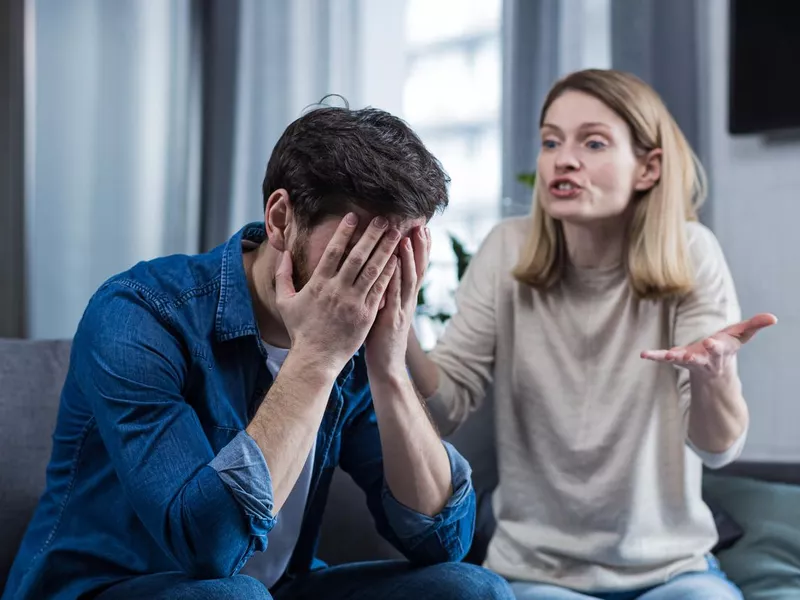 Family conflict, quarrel, misunderstanding. The woman shouts at her husband, in despair, crying. requires explanation. The man listens, covering his face with his hands. Sitting on the couch at home.