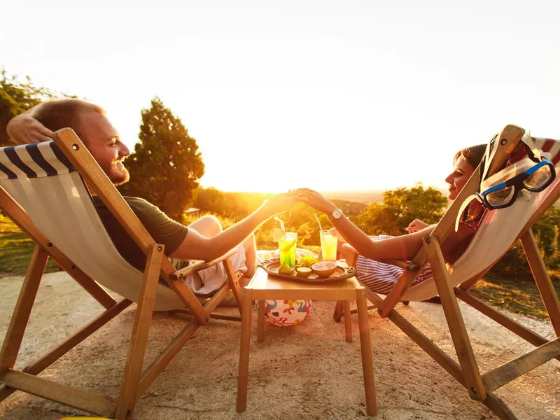 Young couple enjoying summer day on deck chairs with cocktails