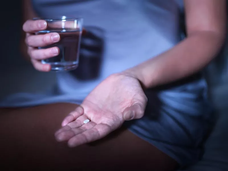 Woman sitting on bed with sleep aid pill