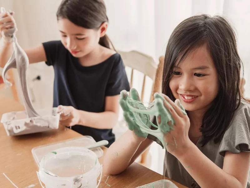 Happy mixed Asian girl friends making homemade slime toy, sensory art and craft, fun homeschool chemistry project