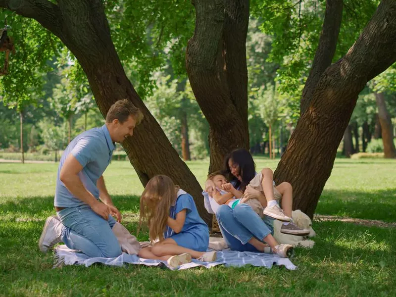 Cheerful parents tickling kids on picnic. Family amusement on summer weekend.