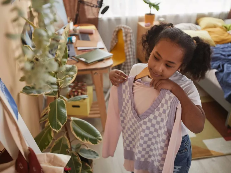 Black girl trying on clothes by mirror in room