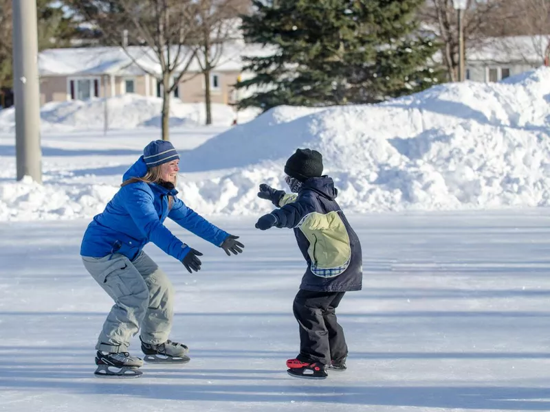 Mother waiting with arms opened her son to help him ice skating