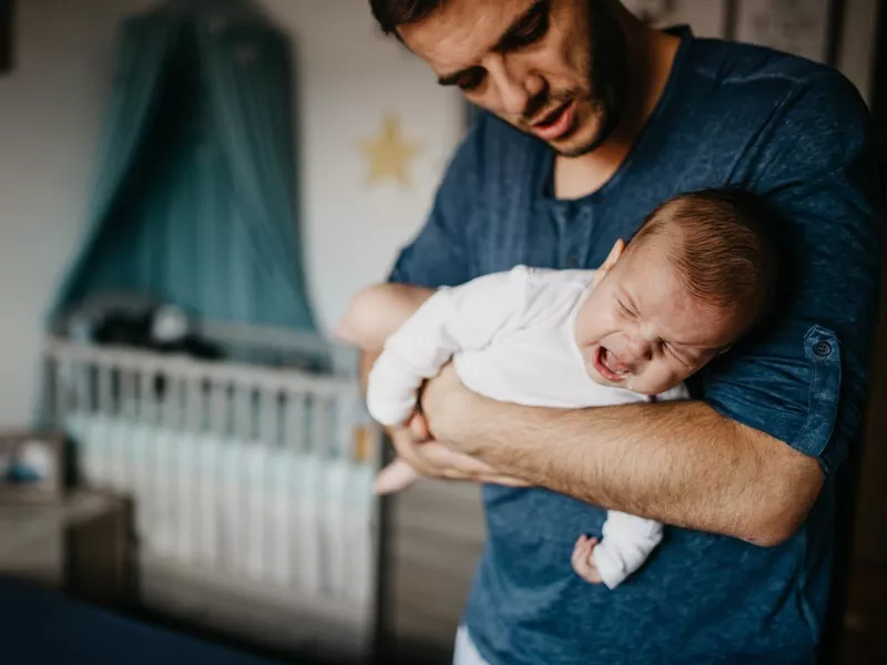 Dad holding crying baby in the colic carry