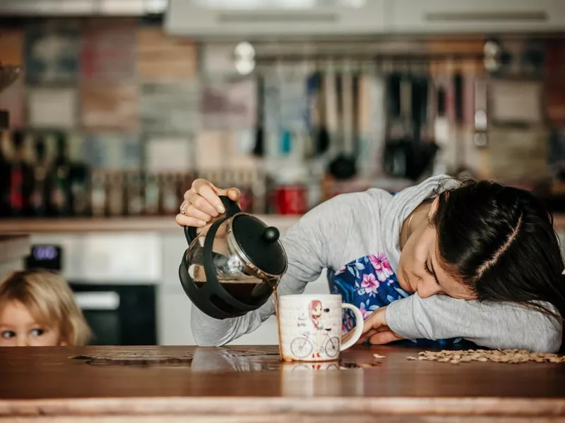 Tired mother, trying to pour coffee in the morning. Woman lying on kitchen table after sleepless night