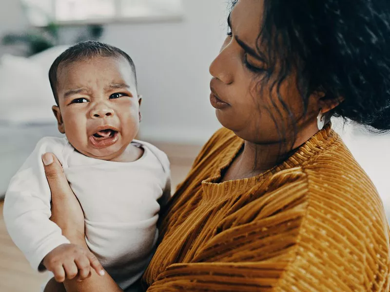 Baby boy crying while his mother carries him at home