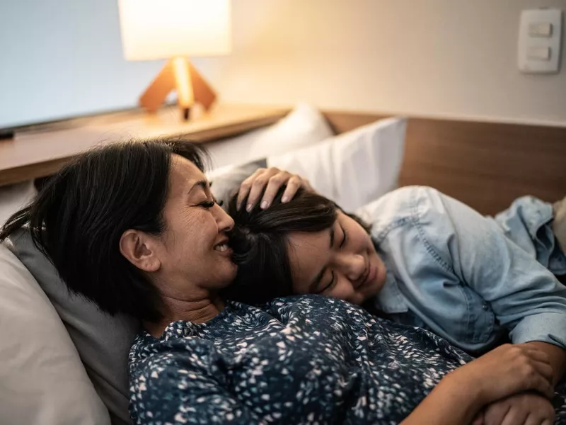 Mother laying down with daughter in bed at home