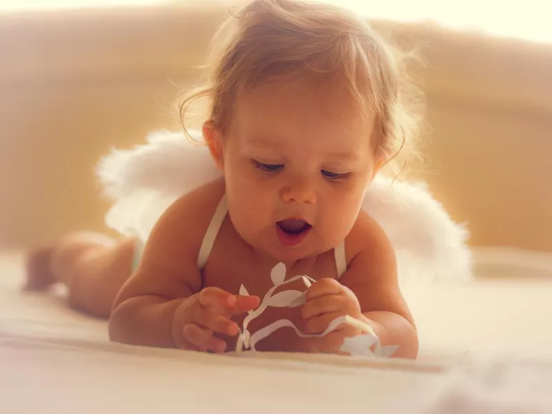 Baby girl with angel wings playing on bed