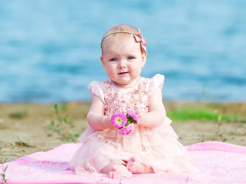 Baby in a pink dress sitting on a river bank