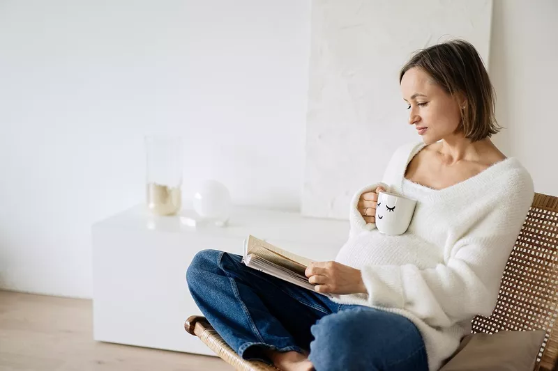 Pregnant woman sitting in an armchair and reading a book