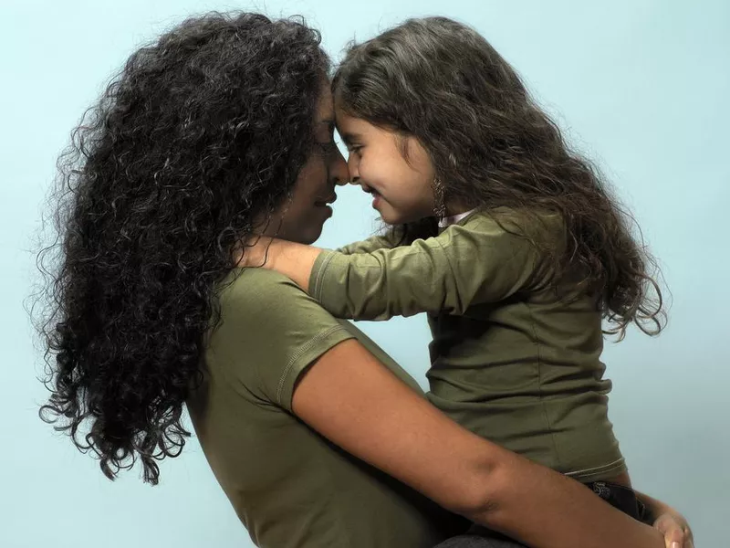 Mother carrying daughter head to head, side view