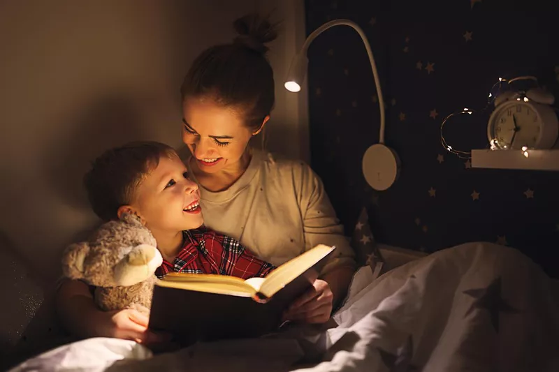 Cheerful mother and son cuddling and reading book