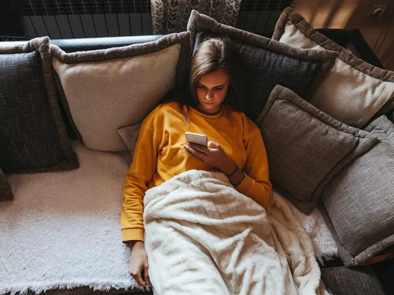 Young woman lying on sofa and using cell phone at home