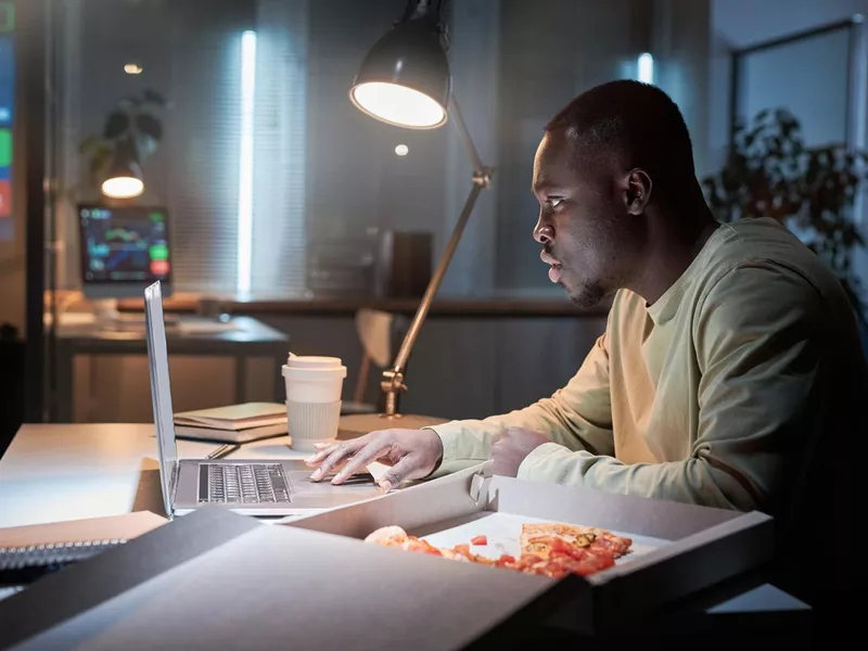 Man working at office eating pizza late at night