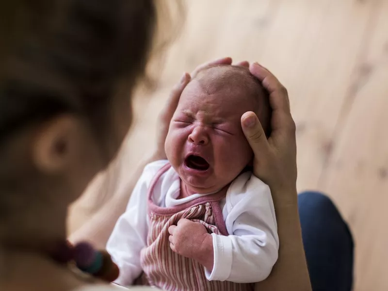 Unrecognizable mother holding crying newborn baby girl.