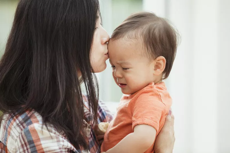 Mother kissing her upset baby to comfort him and stop him from crying