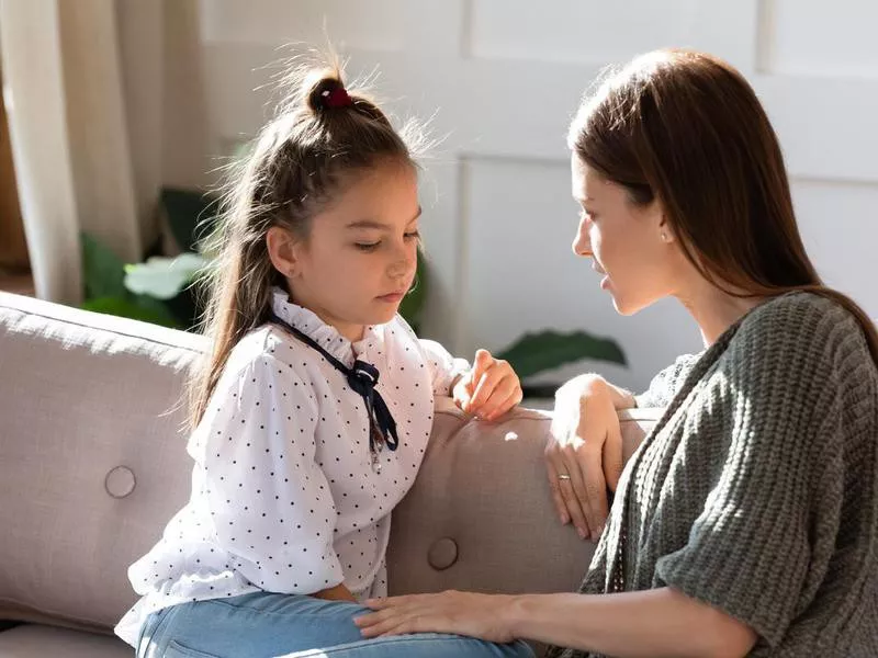 Upset small schoolgirl having trustful conversation with mother.