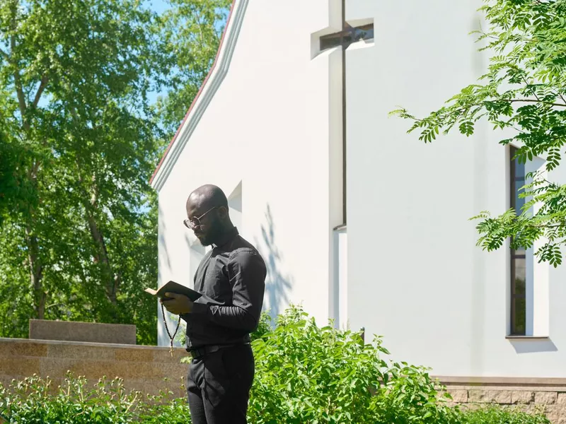 Side view of young preacher in black clothes looking at open Holy Bible