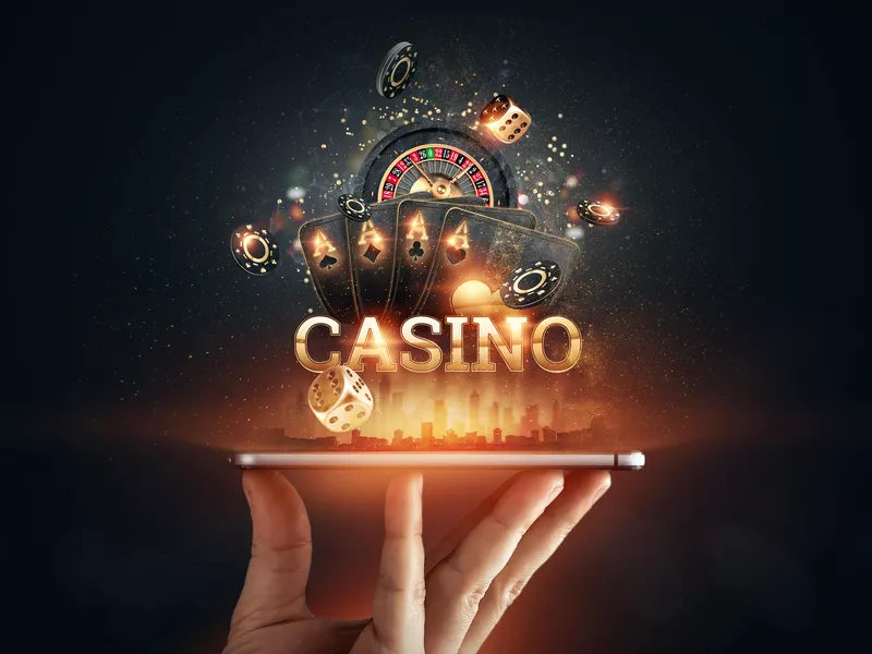 Hand holding a smartphone with playing cards, roulette, chips at online casino