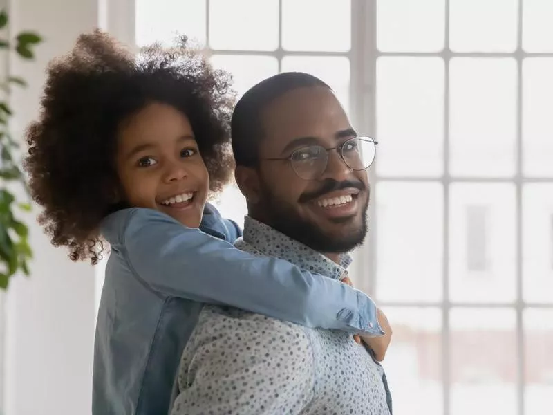 Portrait of happy African American daddy piggy backing cute daughter