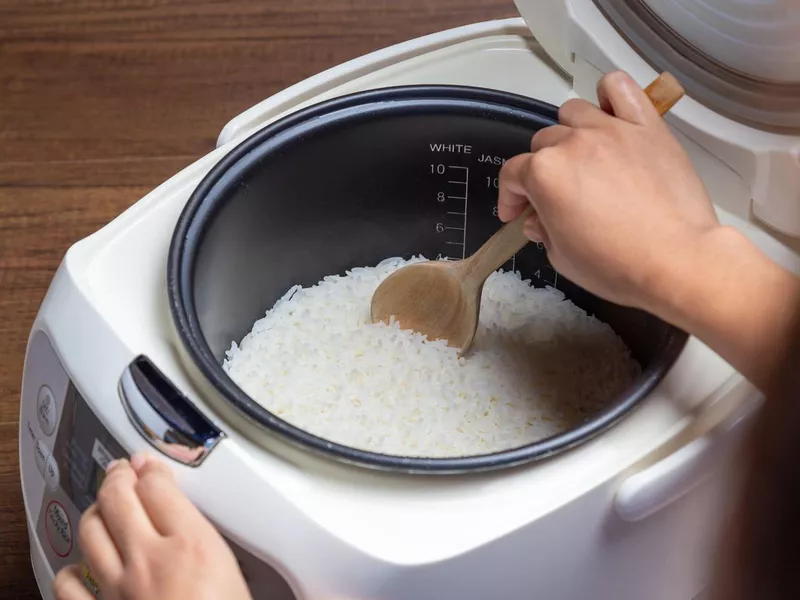 Woman hand is scooping jasmine rice cooking in electric rice cooker with steam. Thai Jasmine rice.