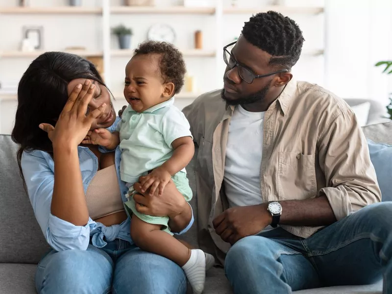 Tired parents with crying kid on sofa