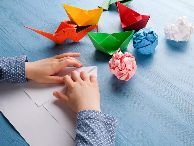 The child at the table makes origami from colored paper.