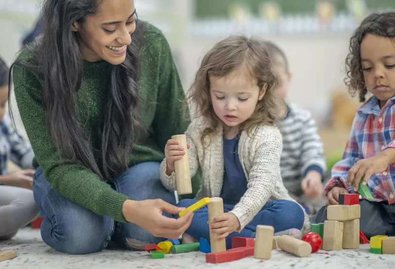 Preschool children playing in a classroom with a teacher