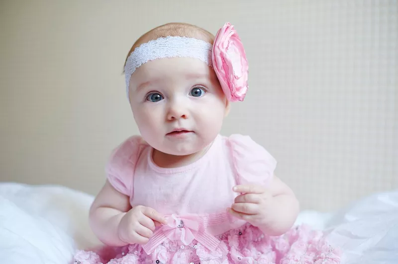 Cute baby girl sitting on a bed wearing pink