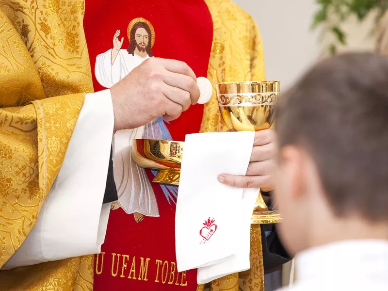 The priest gives first communion. Symbol of the body and blood of Jesus.