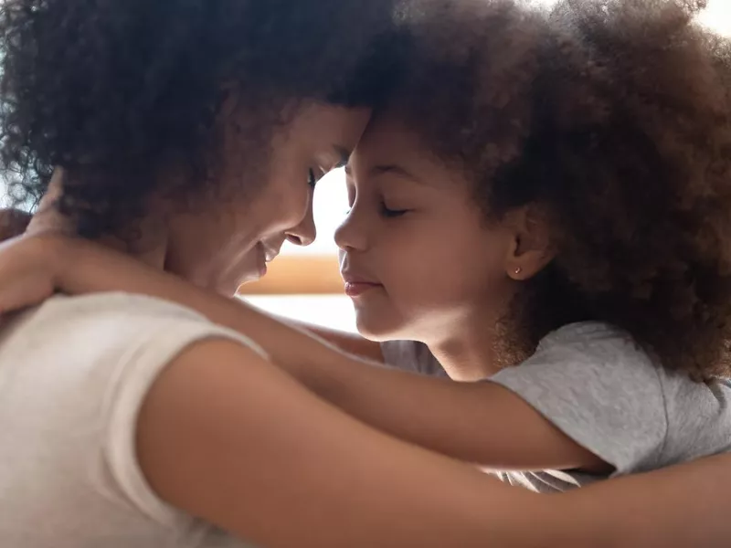 Mixed race mother touching foreheads with little cute daughter.