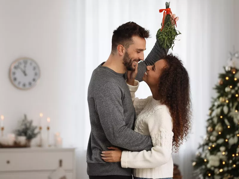 Lovely couple under mistletoe bunch in room decorated for Christmas