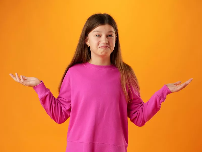 Puzzled teen girl don't know what to do on yellow background in studio