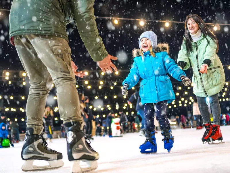 Skating rink. Happy family on the ice rink. Mom and dad teach daughter to skate.