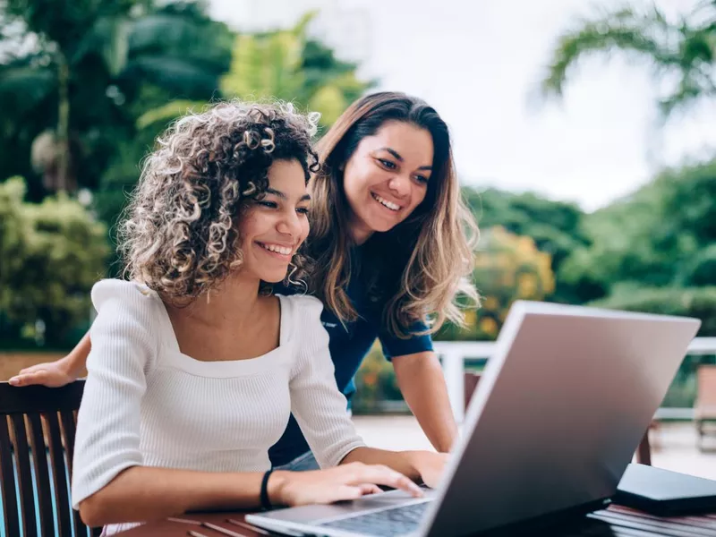 Mother and daughter using laptop at swimming pool area