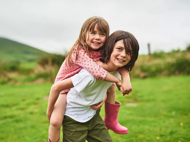 Portrait of a little boy giving his sister a piggyback ride outdoors