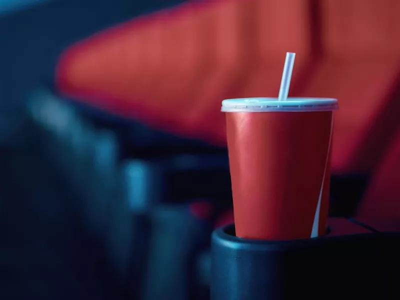 Selective focus on empty disposal cup of soda with red cinema seats in the background