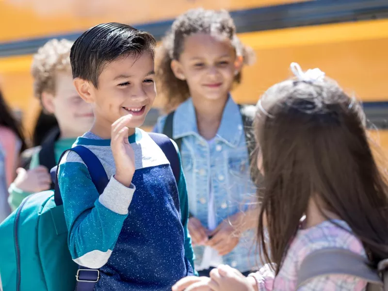 School boy shyly waves at a girl at the bus stop