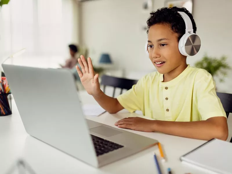 Boy using laptop and waving during video call while homeschooling