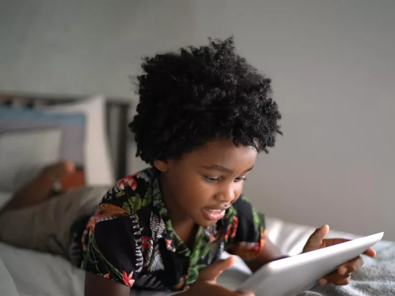 Boy lying in bed playing games on digital tablet at home