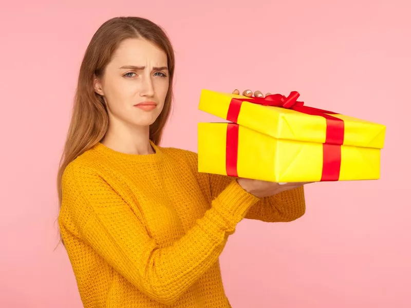 Portrait of unhappy red hair girl in sweater opening gift box and looking sadly at camera, disappointed with birthday surprise