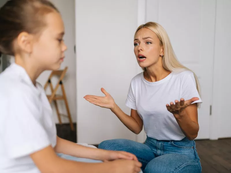 Close-up side view of angry emotional young mother scolding, raising voice, scream and gesturing with hands at stubborn difficult little child daughter at home.