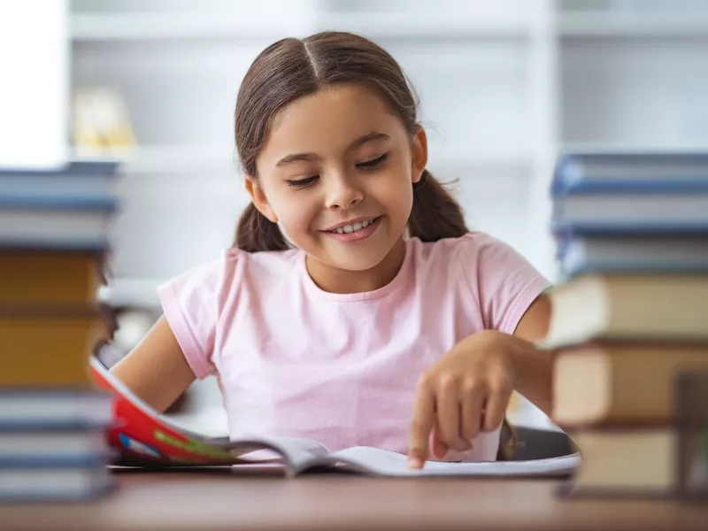 Happy schoolgirl sitting at the desk with a books