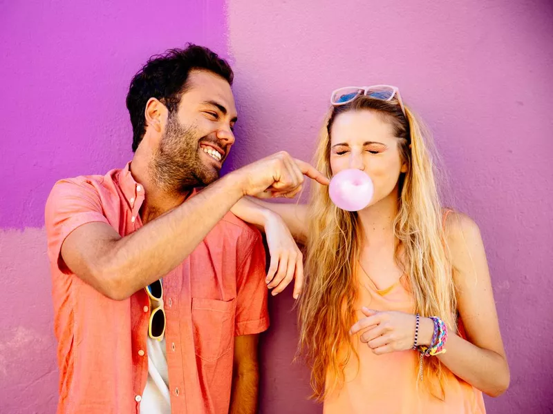 Playful man popping chewing gum bubble of girl