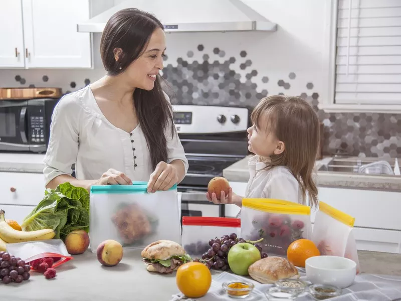 Mother and daughter pack sandwiches and fresh food into clear storage bags