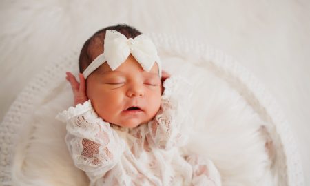 Newborn baby girl sleeps in a white round basket covered with fur blanket; white background