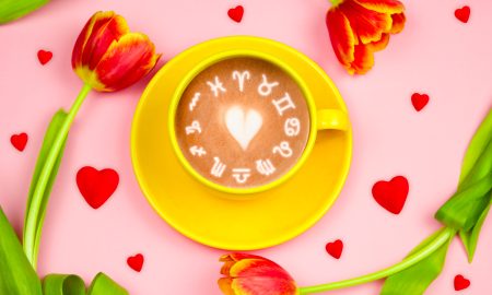 Top view yellow  coffee cup with zodiac signs on pastel pink background.